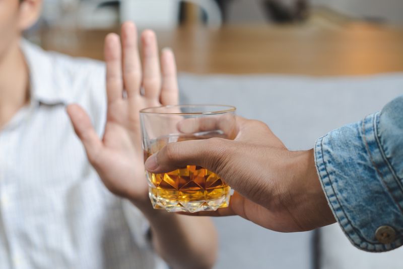 hand offers glass containing alcoholic spirit to person holding up their hand to refuse