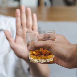 hand offers glass containing alcoholic spirit to person holding up their hand to refuse
