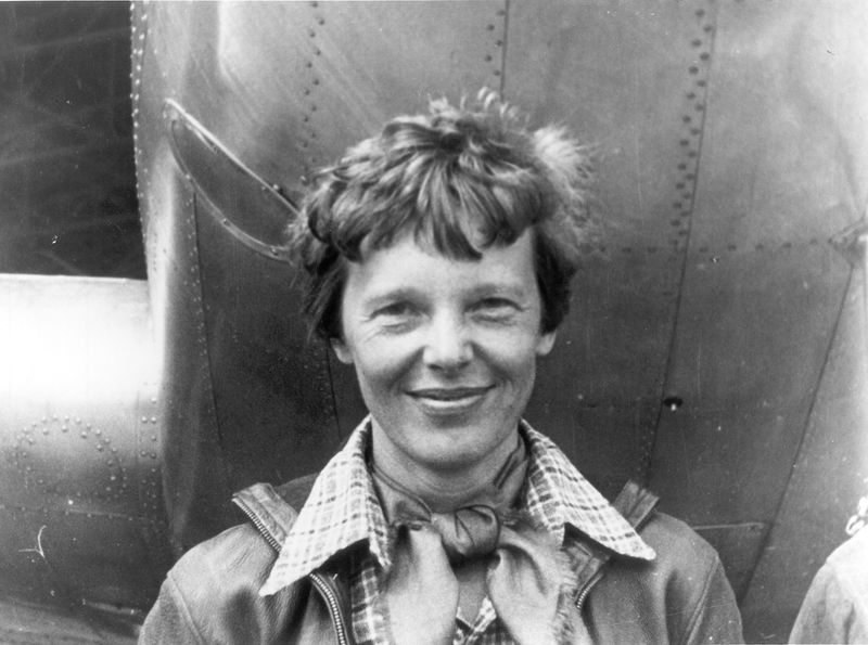 A black and white photo showing Amelia Earhart standing by her plane. 