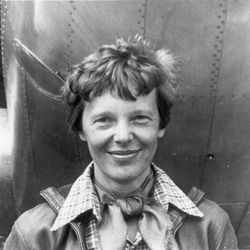 A black and white photo showing Amelia Earhart standing by her plane. 