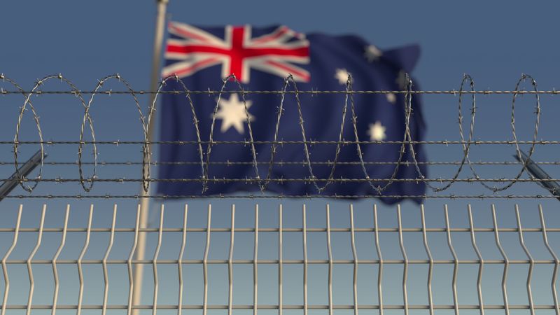 Blurred waving flag of Australia behind barbed wire prison fence. 