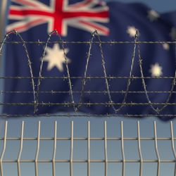 Blurred waving flag of Australia behind barbed wire prison fence. 