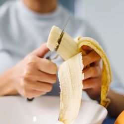 A woman sitting by the table at home cutting banana.