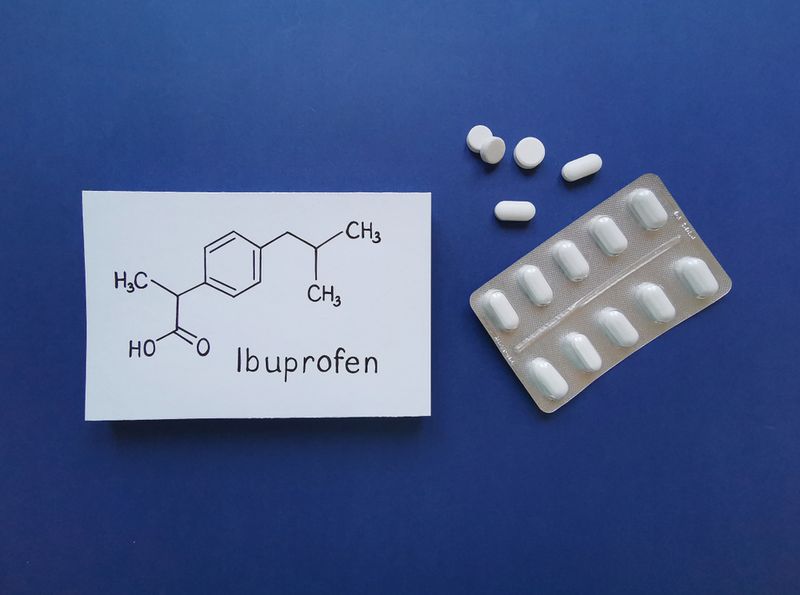 Blister packet of white pills next to a drawing of Ibuprofen's structure on a blue background