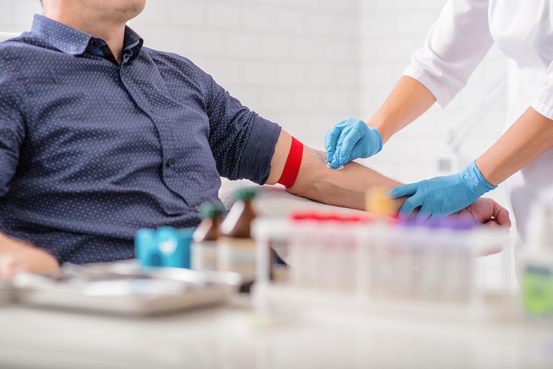 clinician disinfects man's arm before blood is taken, with medical equipment out of focus in the foreground