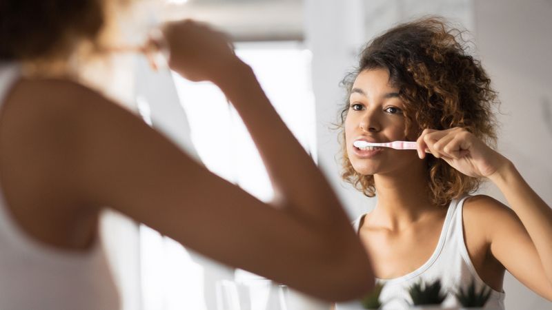 A woman brushing her teeth in the mirror.