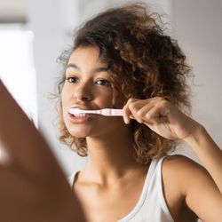 A woman brushing her teeth in the mirror.