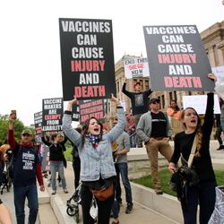 A group of Americans protesting vaccines while looking angry and holding angry looking signs. 
