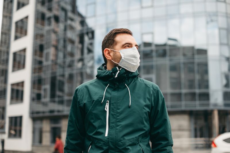 A photo of a man in a green jacket wearing a white face mask. 