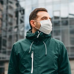 A photo of a man in a green jacket wearing a white face mask. 