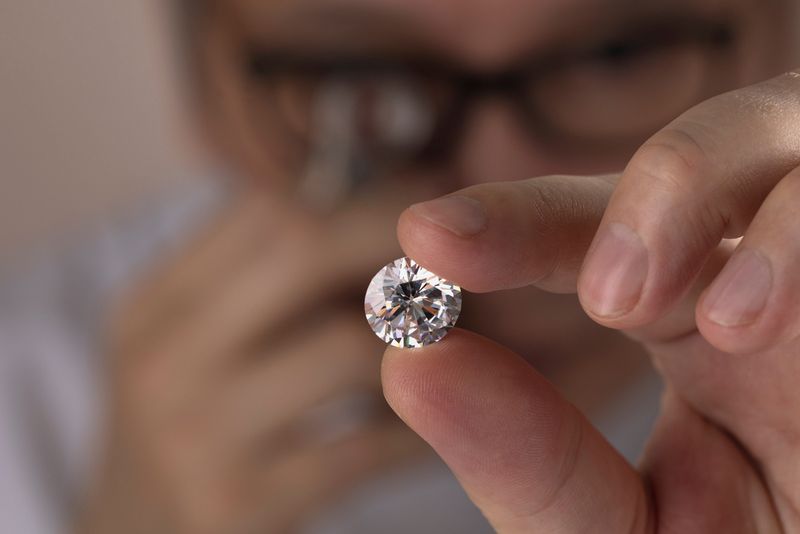  man expert buyer with glasses evaluates polished diamond trough magnifying glass close up.