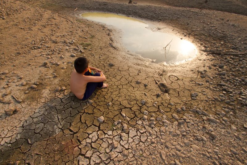A boy sitting by a dried up water reserve. 