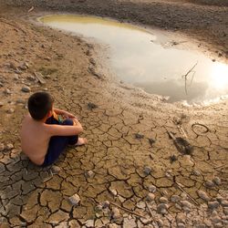 A boy sitting by a dried up water reserve. 