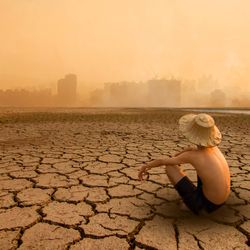 Young man sitting on drying river and looking to polluted city with smoke of co2, carbon dioxide on background.