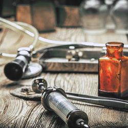 Retro syringe, stethoscope and medical cupping glass on a wooden table. Shallow depth of field. Vintage style.