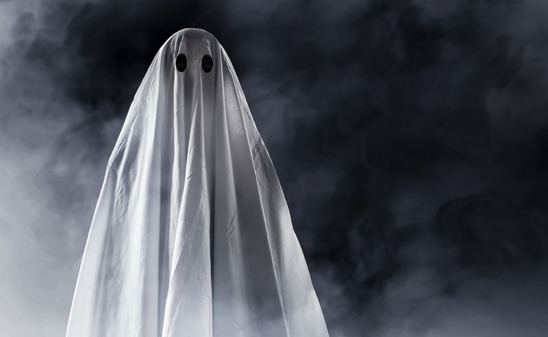 A ghost costume consisting of someone standing under a sheet with holes for eyes 
