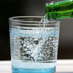 Green glass bottle pouring sparkling water into a glass