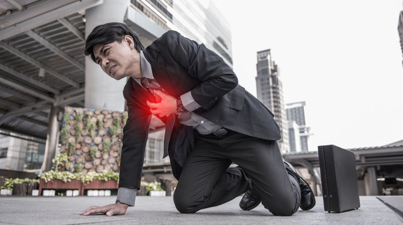Man in suit bent over on pavement clutching his chest