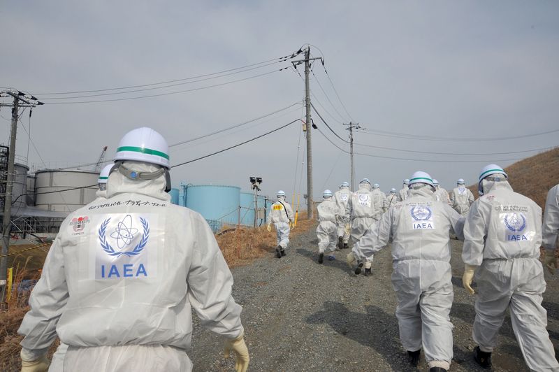 A team of IAEA inspectors visit the Fukushima site in 2015. They are wearing safety suits with the IAEA logo on their backs. 