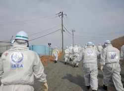 A team of IAEA inspectors visit the Fukushima site in 2015. They are wearing safety suits with the IAEA logo on their backs. 