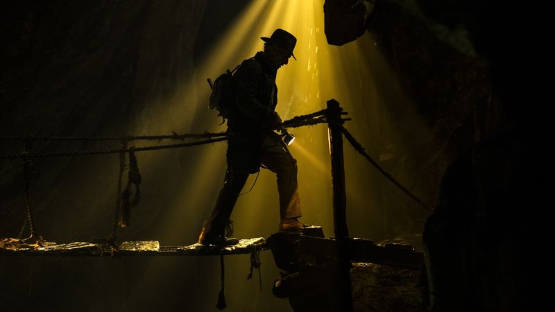 A screen shot of Indiana Jones crossing a bridge. His image is silhouetted against a yellow light. 