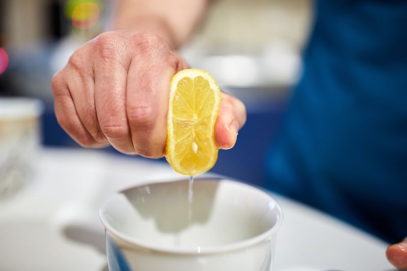 Man's hand squeezing half a lemon into a bowl