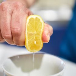 Man's hand squeezing half a lemon into a bowl