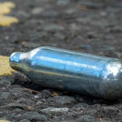 A discarded nitrous oxide cannister sits on a tarmac road.