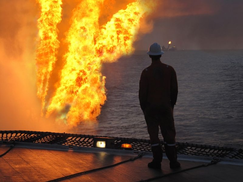 Silhouette of a oil rig worker watches as a fire bursts from the platform over the sea. 