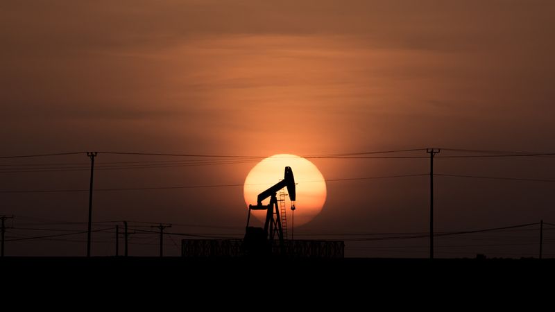 Silhouette of an oil drill in front of a setting sun horizon. 