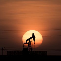 Silhouette of an oil drill in front of a setting sun horizon. 