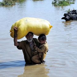 A farmer holding a boy and sack is up to his waist in flood waters in Pakistan
