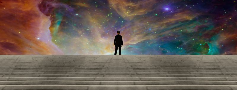 Person in black suit at the top of stairs facing a rainbow nebula