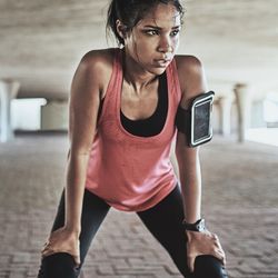 Person in pink tank top and phone strapped to their arm, resting after exercise while looking sweaty
