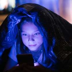 A teen girl under the cover looking at a phone.