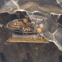 An ancient pizza, proto-pesto, wine, and fruit can be seen on the Roman platter.