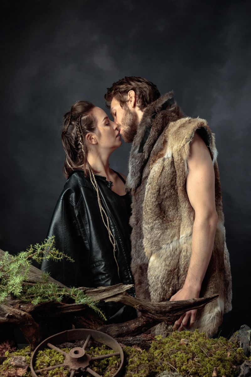 Post-apocalyptic couple kissing, dressed in fur, on a black background
