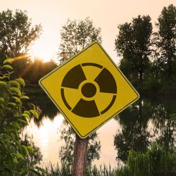 Radioactive pollution. Yellow warning sign with hazard symbol near contaminated area outdoors