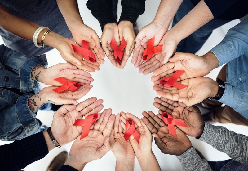 Group of hands holding red ribbonsymbolizing HIV/AIDS awareness
