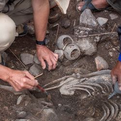 A photo of the researchers examining the shaman's remains as well as some of the ceramic objects that were buried with him. 