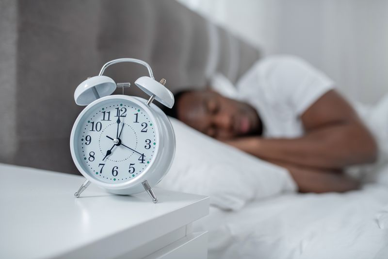 man sleeping with analog alarm clock in foreground