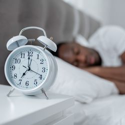 man sleeping with analog alarm clock in foreground