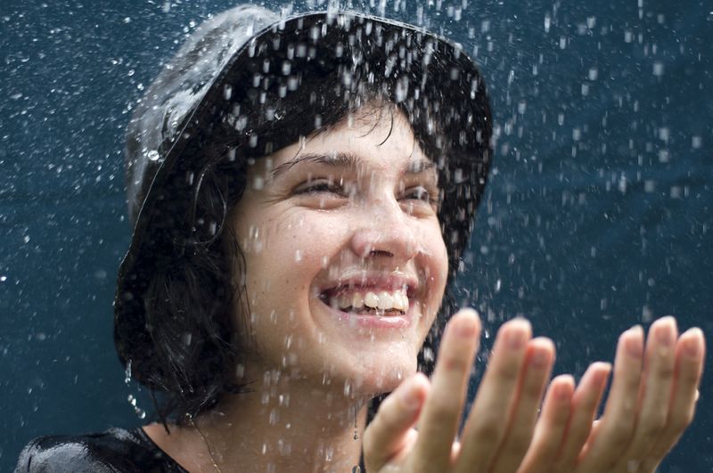 A woman in a bad hats holds her hands in front of her as she enjoys the rain. 
