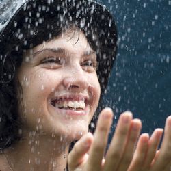 A woman in a bad hats holds her hands in front of her as she enjoys the rain. 