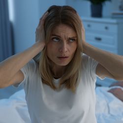 woman covering ears while man snores in bed in background