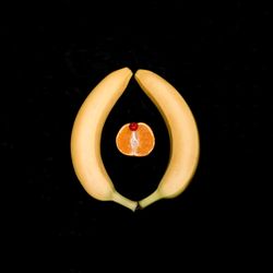 two bananas, an orange, and a cherry representing a vulva and clitoris on a black backround.