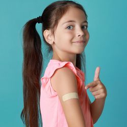 An image of a little girl showing off a plaster/band aid on her arm from an injection.  