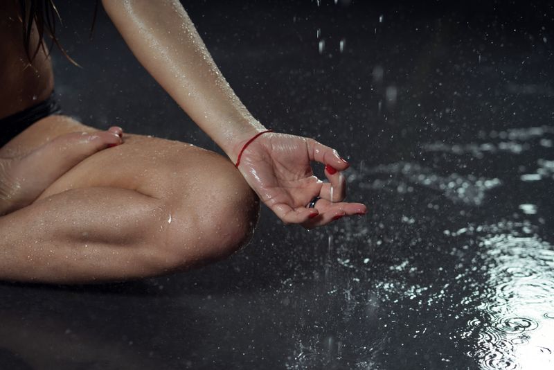 View of a person's knee and hand while they hold a lotus pose in the rain