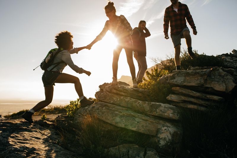 Four people climbing up a rock against a low sun background. 