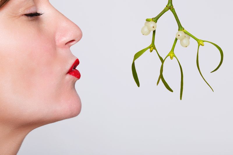 Woman kissing mistletoe on white background